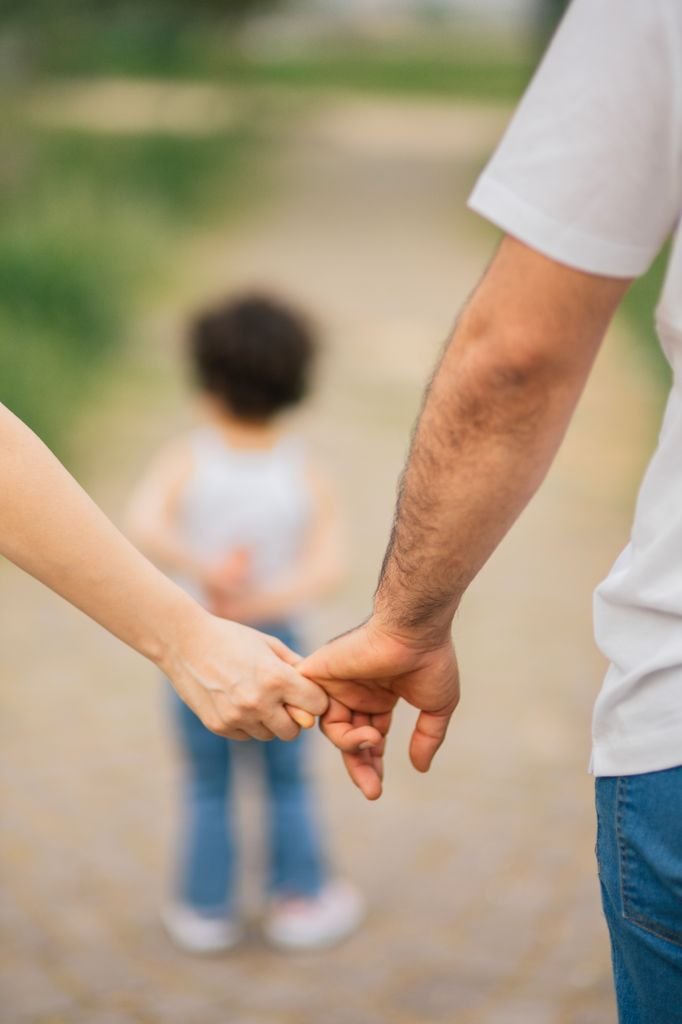 Parents holding hands walking with their child outdoors on a sunny day.